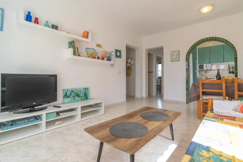 Una sala de estar con televisión, mesa baja y un arco que da al comedor.