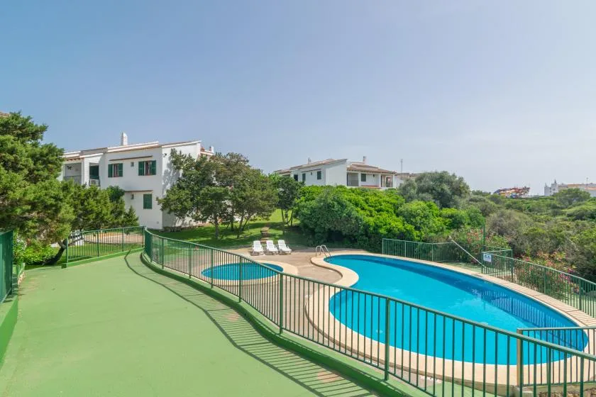 Una piscina al aire libre está junto a una zona pavimentada verde y árboles.