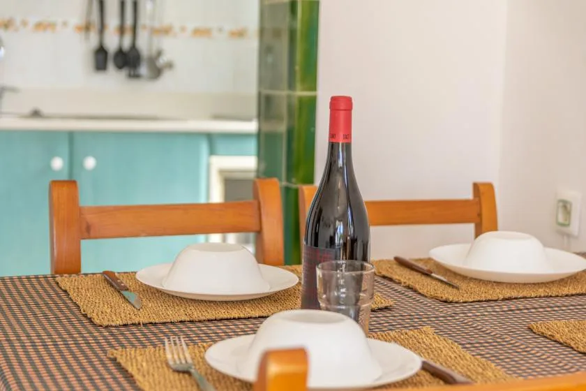 Una mesa de comedor está preparada con platos, individuales tejidos y una botella de vino.