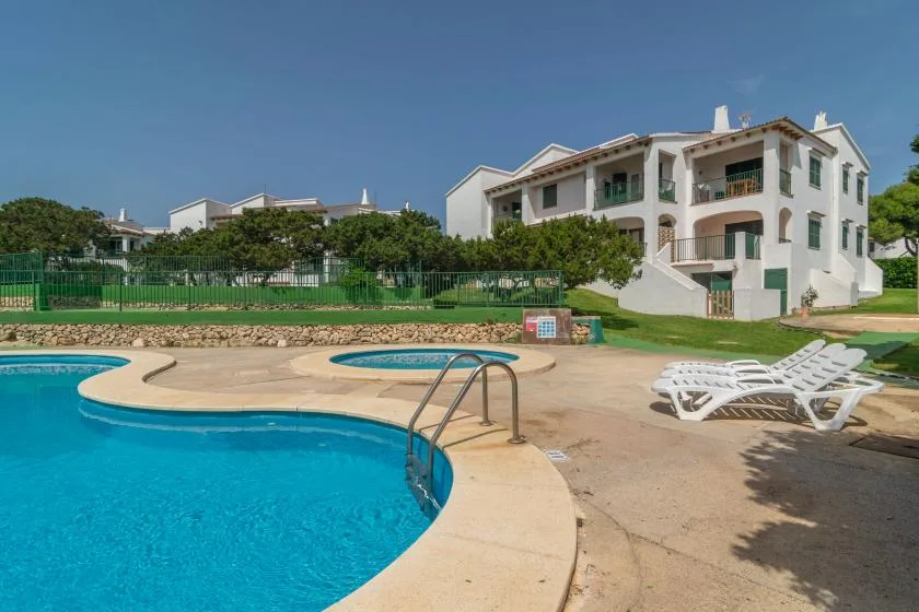 Una piscina al aire libre junto a un edificio blanco de varios pisos.