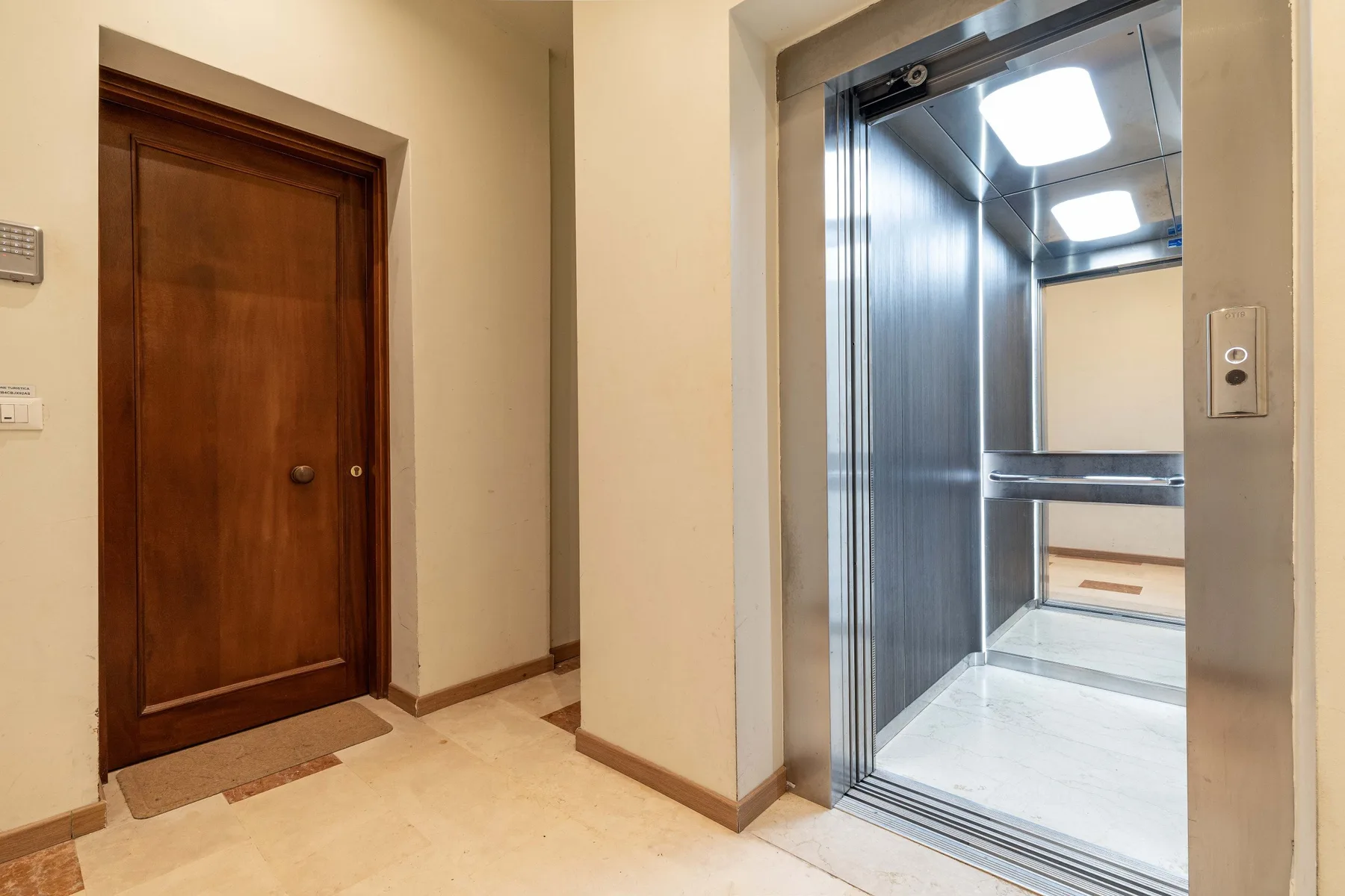 Un pasillo interior con una puerta de madera junto a un ascensor abierto.