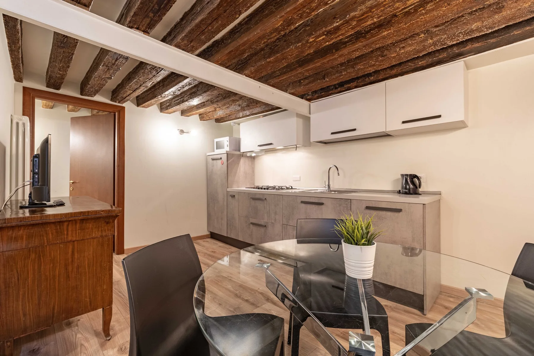 Una cocina pequeña y comedor con gabinetes grises y una mesa de vidrio.