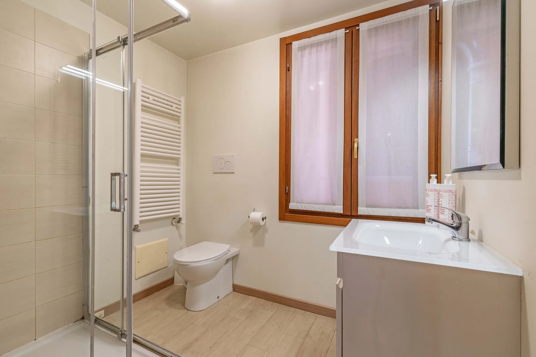Un baño con ducha de vidrio, inodoro y lavabo bajo una ventana.