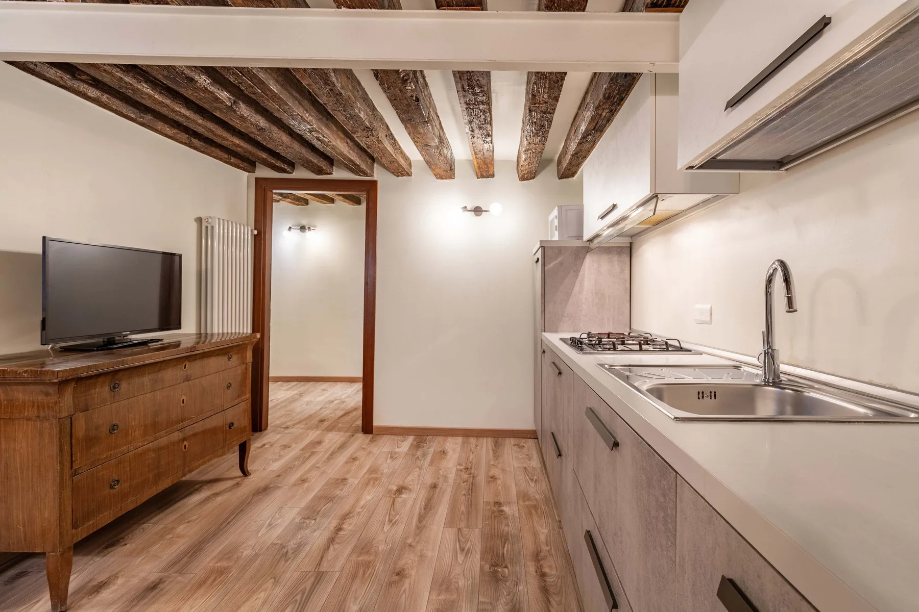 Una cocina compacta con encimera, fregadero y televisor sobre un mueble de madera.