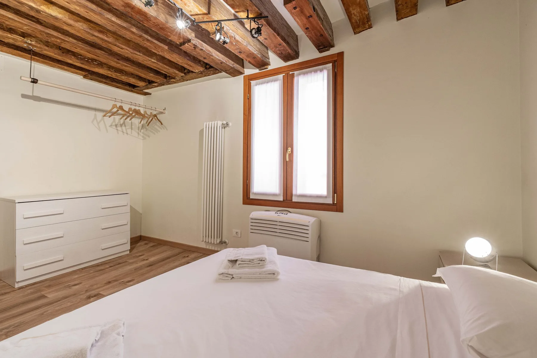 Un dormitorio con una cama, vigas de madera en el techo y una ventana.