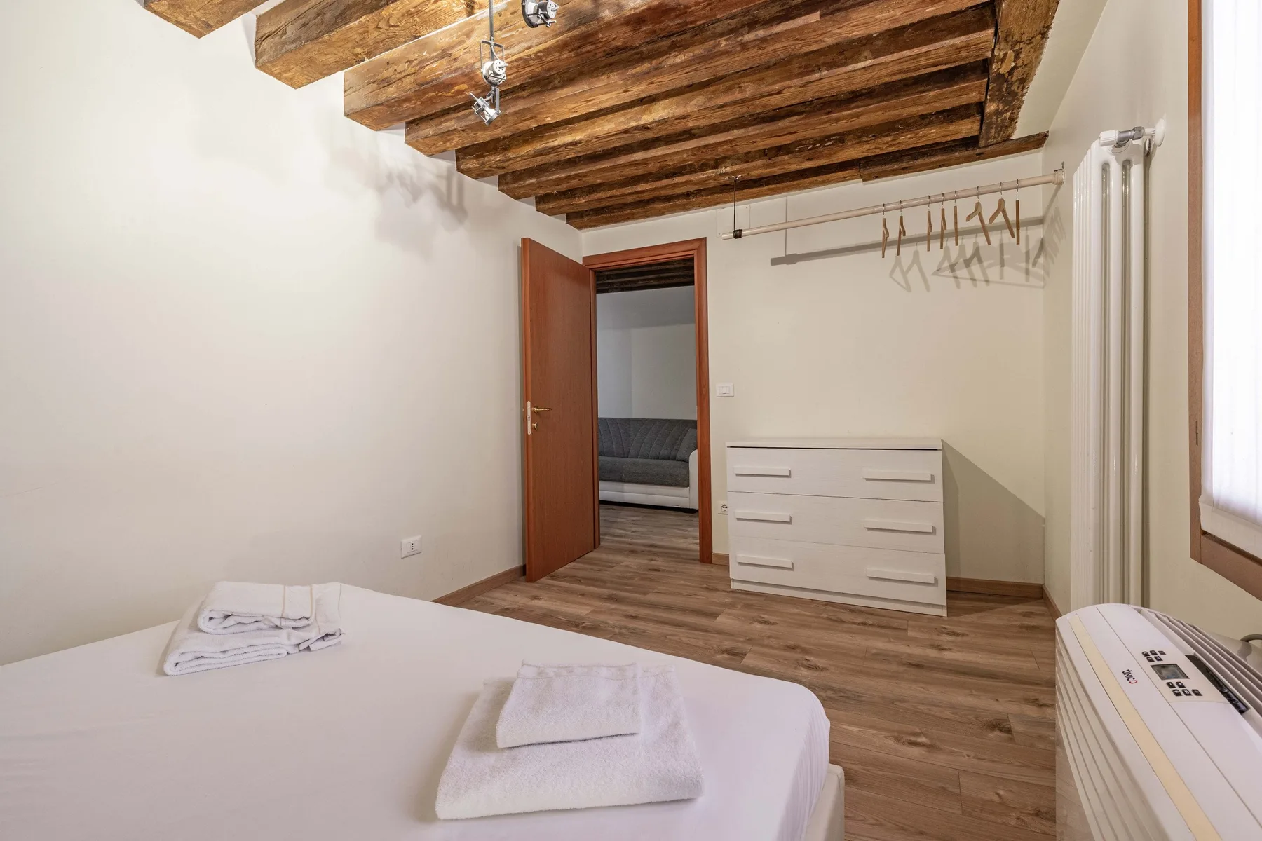 Un dormitorio con una cama, toallas dobladas, una cómoda y vigas de madera vistas en el techo.