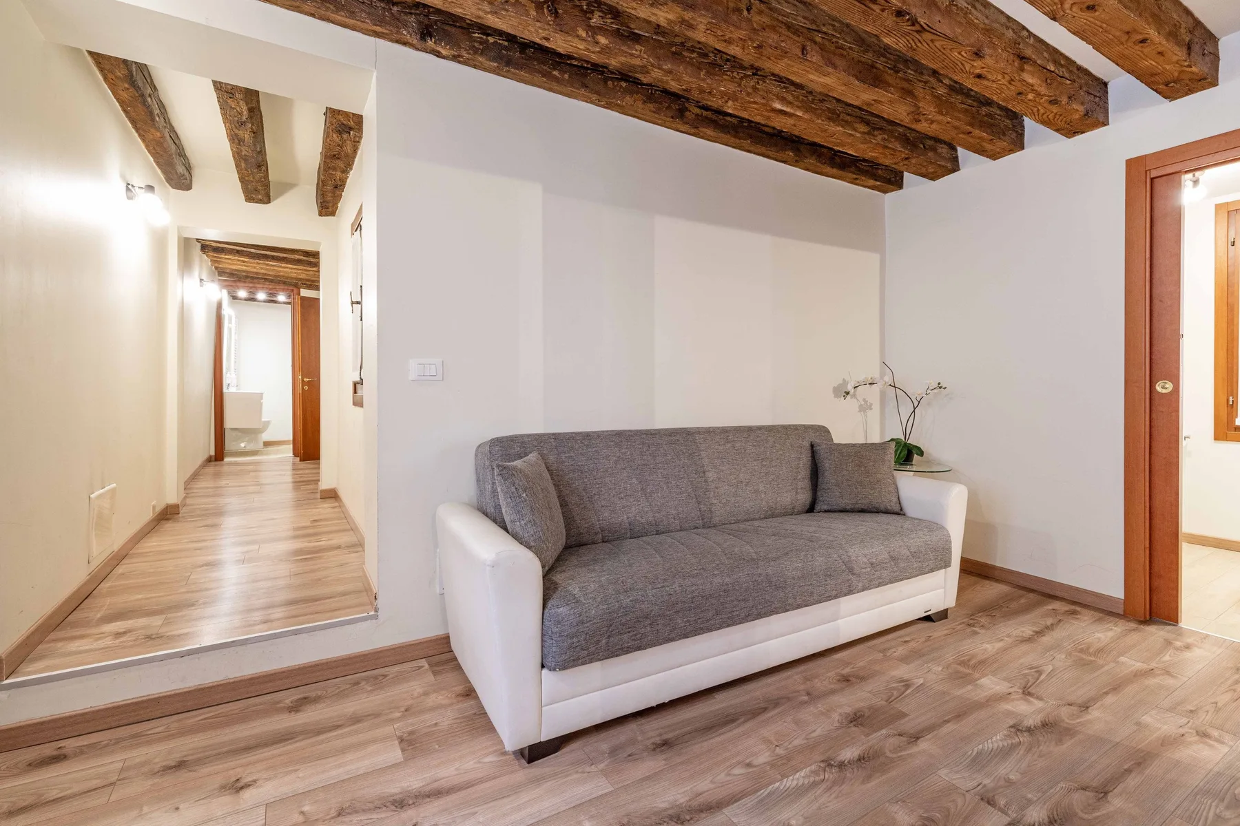 Una sala de estar con un sofá gris bajo vigas de madera expuestas.