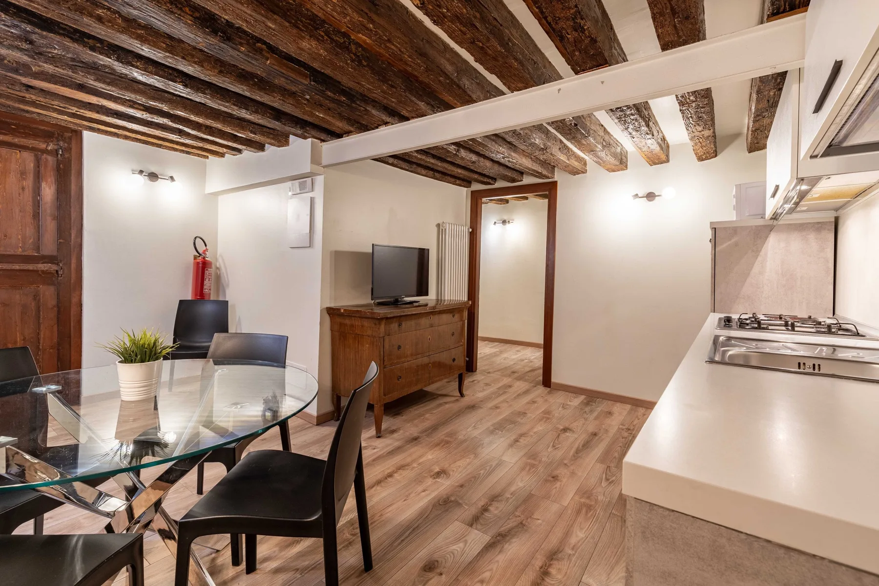 Comedor y sala de estar con mesa de vidrio, televisor y vigas de madera expuestas en el techo.