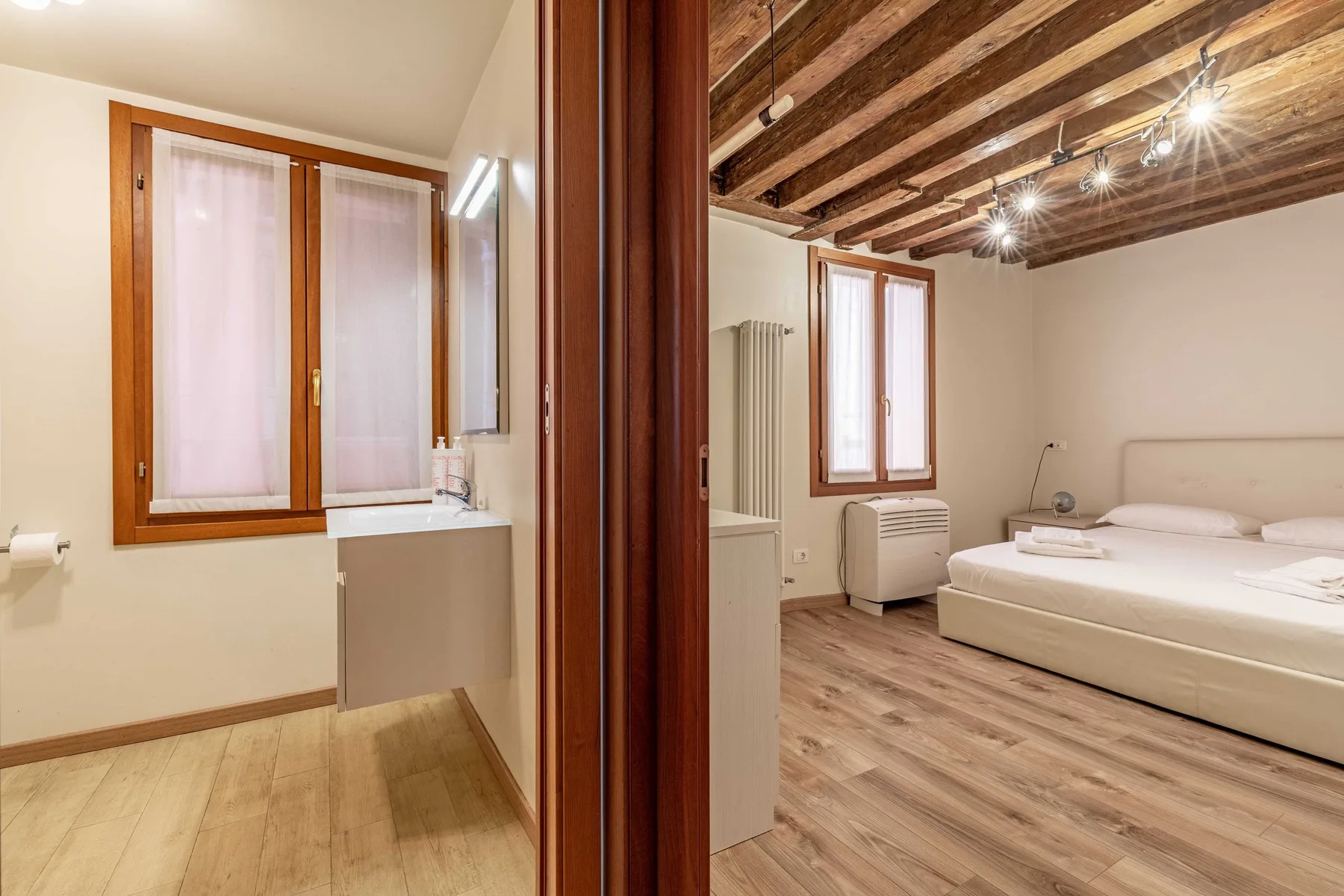 Un dormitorio con cama y techo de vigas de madera, junto a un baño.