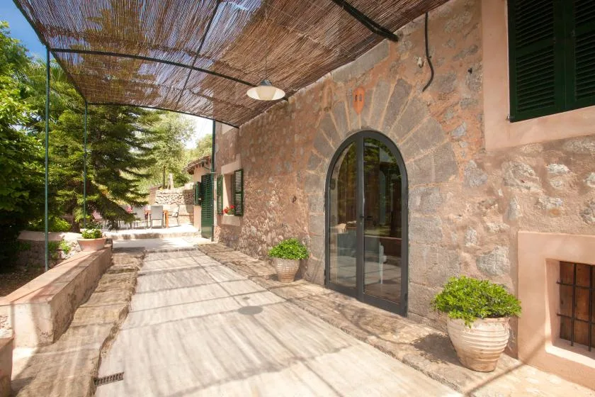 A stone terrace runs beside an arched glass doorway beneath a woven canopy.