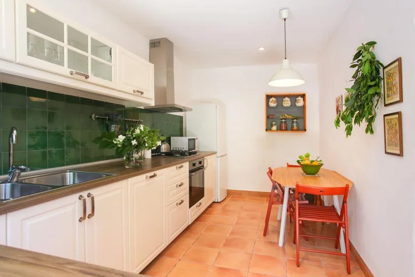 A bright kitchen with a long counter, green backsplash, and a dining table.