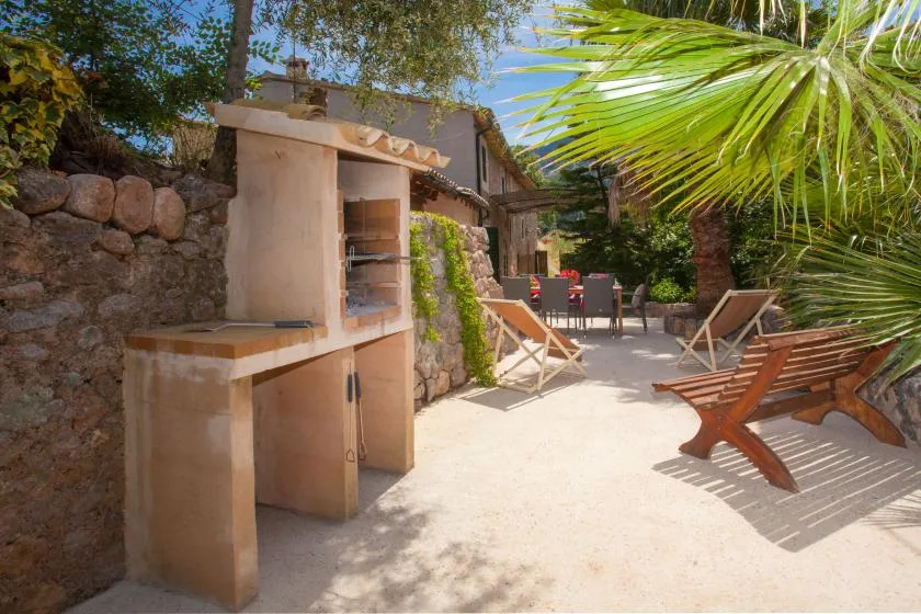 A sunny outdoor patio with a built-in grill, seating, and leafy plants.