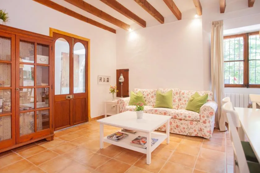 A bright living room with floral seating and exposed wooden ceiling beams.