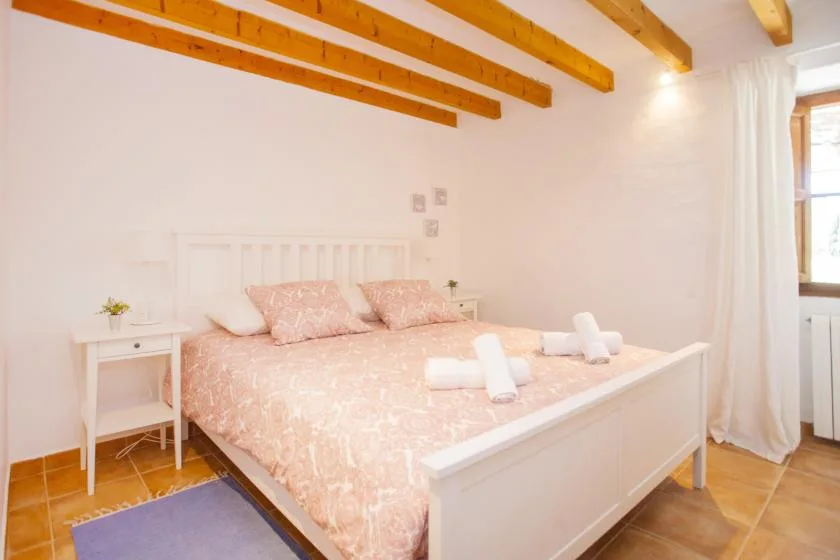 A bedroom with a large bed, pale pink bedding, and exposed wooden ceiling beams.