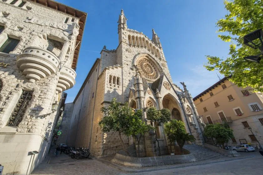 A Gothic stone church with a large circular window stands in a sunlit plaza.