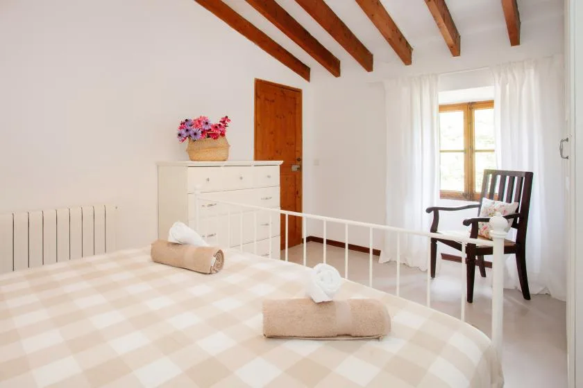 A bright bedroom with a bed, white dresser, and chair beside a window.