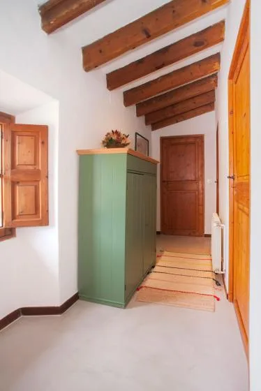 A bright hallway with a green cabinet and exposed wooden ceiling beams.