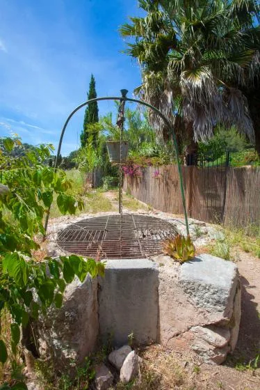 A garden path leads to a circular stone well beneath an arched metal frame.