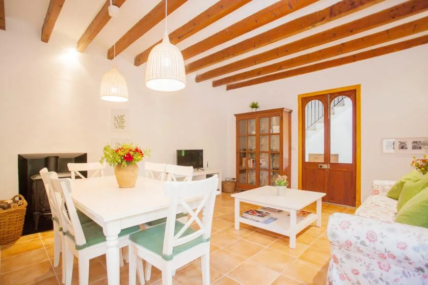 A dining and living room with a white table, wooden ceiling beams, and a glass-front cabinet.