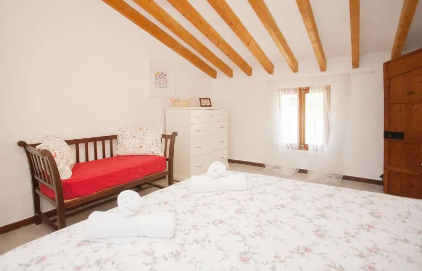 A bedroom with a large bed, a wooden daybed, and a chest of drawers.
