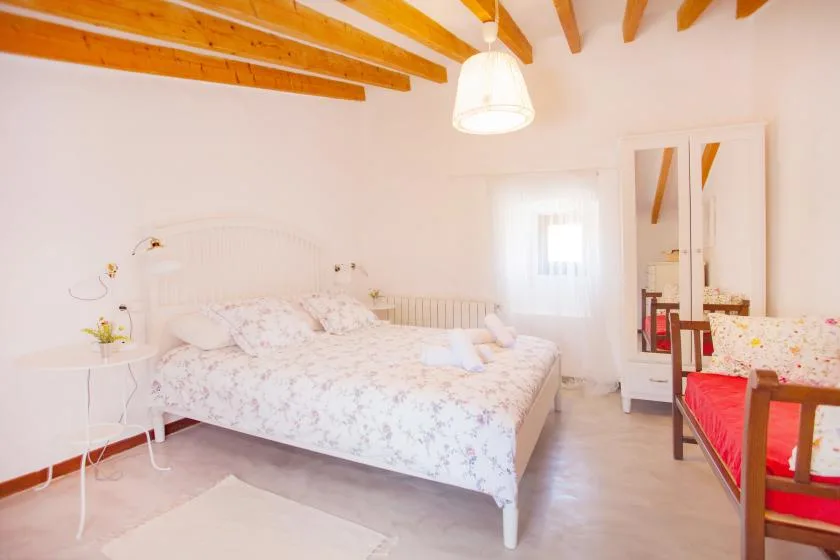 A bright bedroom with a floral bedspread and exposed wooden ceiling beams.