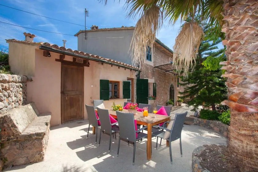A sunny outdoor dining area with a table and chairs beside a stone house.