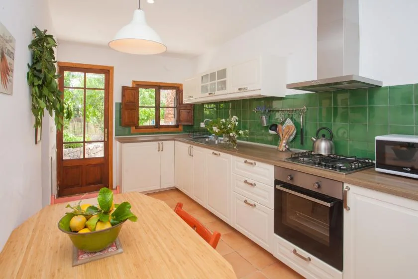A bright kitchen with white cabinetry, green backsplash tiles, and a wooden dining table.