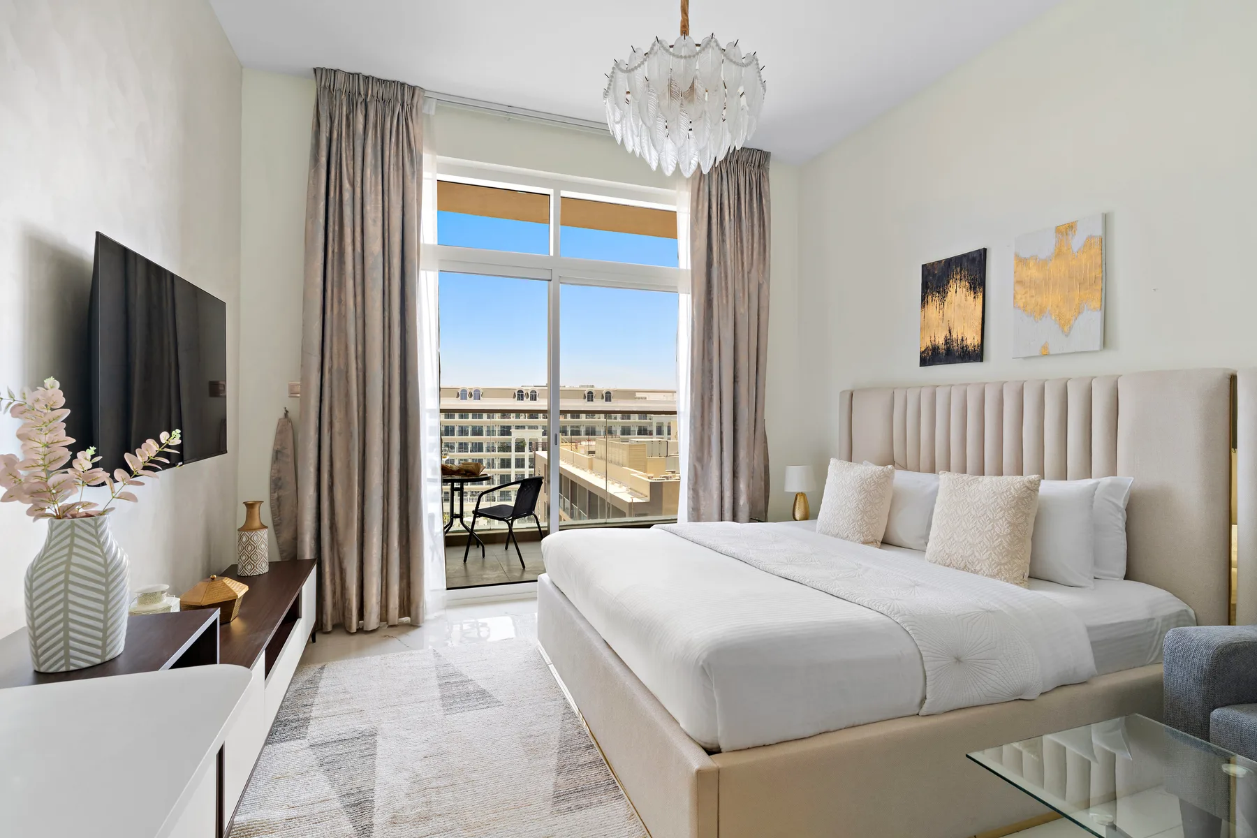 Un dormitorio luminoso con una cama grande junto a una ventana con vistas a edificios cercanos.