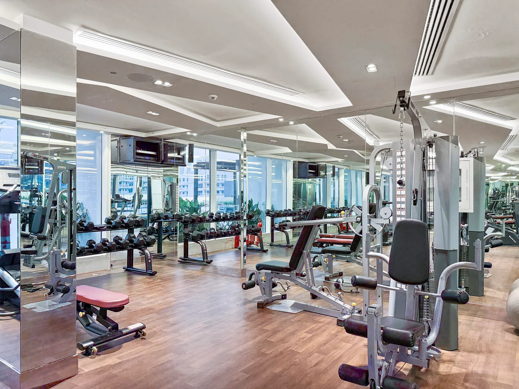 Un gimnasio con máquinas de ejercicio, bancos de pesas y paredes con espejos.
