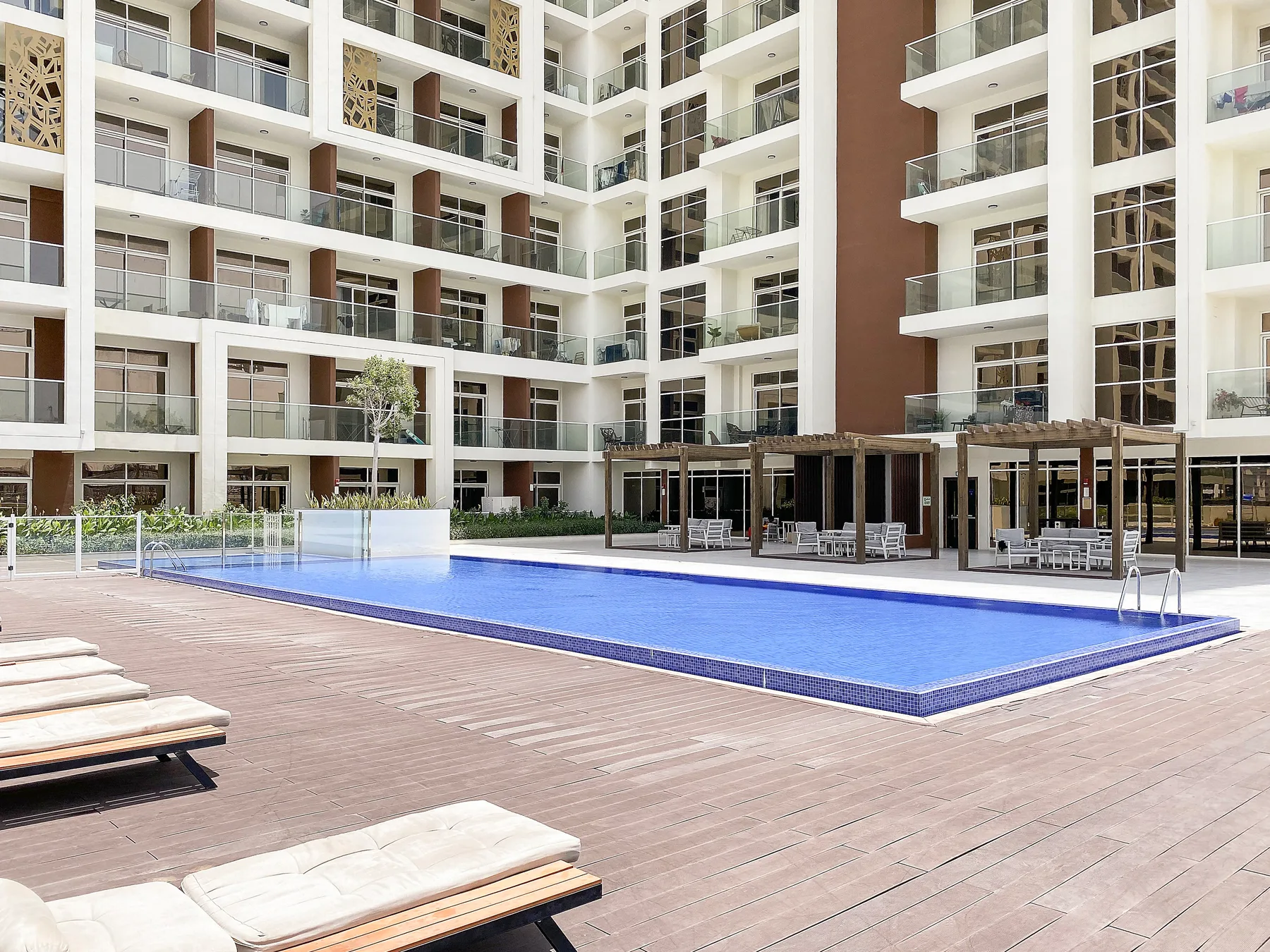Una piscina en un patio está junto a una terraza pavimentada y balcones de apartamentos.