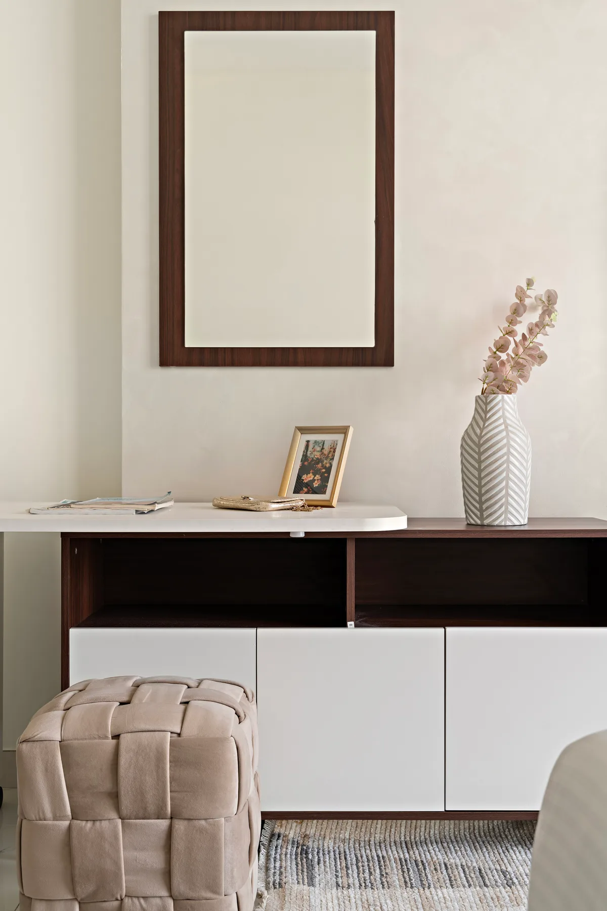 Una habitación luminosa muestra un mueble bajo, arte enmarcado y un jarrón con flores.