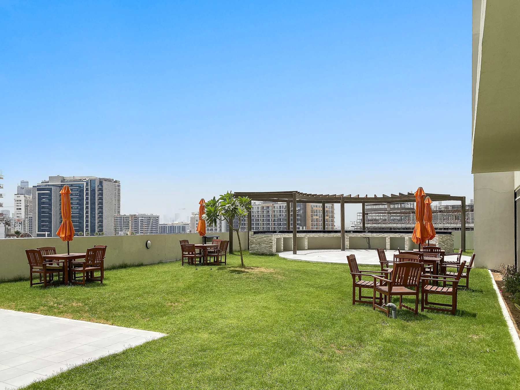 Una terraza en la azotea con césped, asientos al aire libre y sombrillas naranjas.