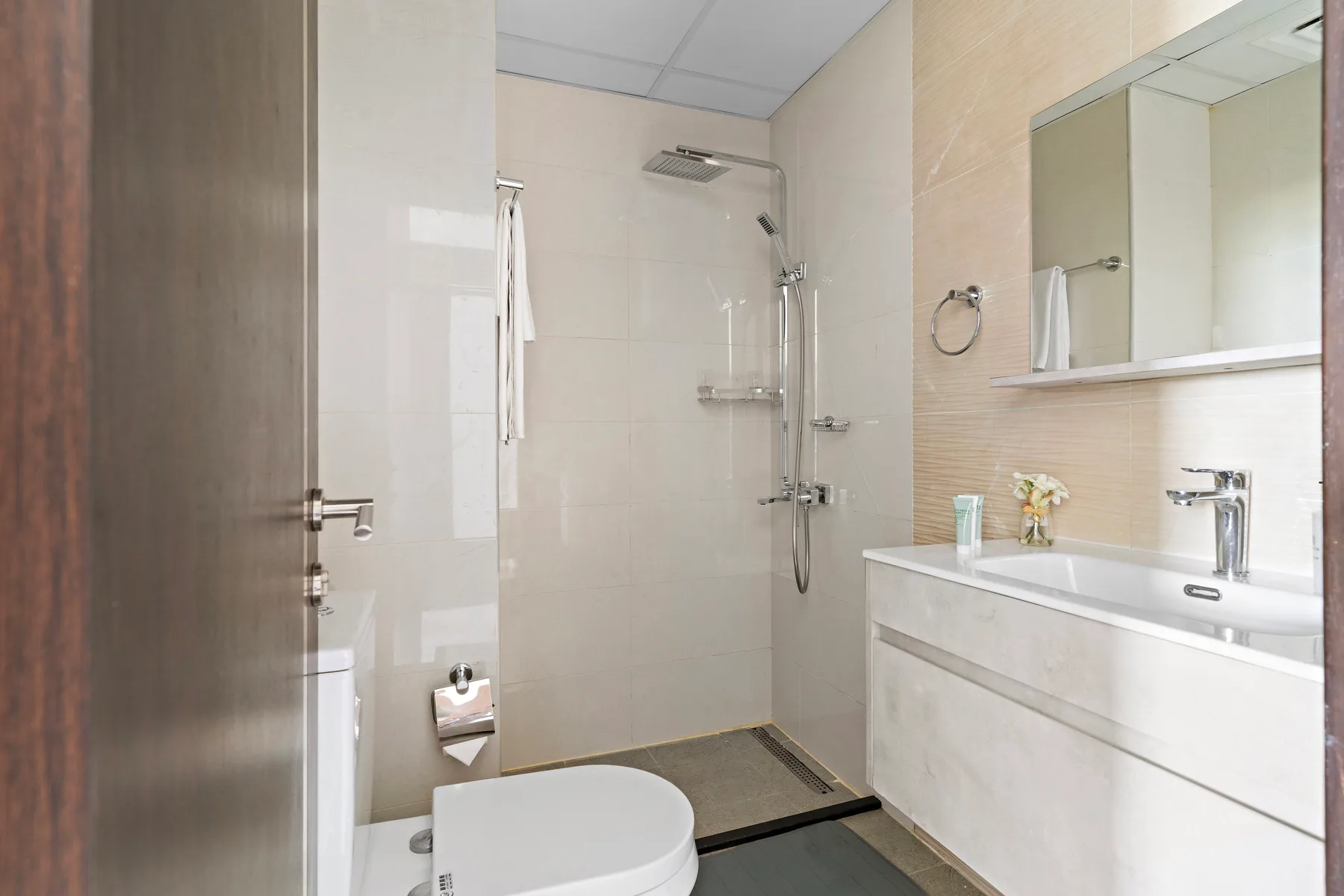 Un baño con ducha, inodoro y lavabo bajo un espejo de pared.