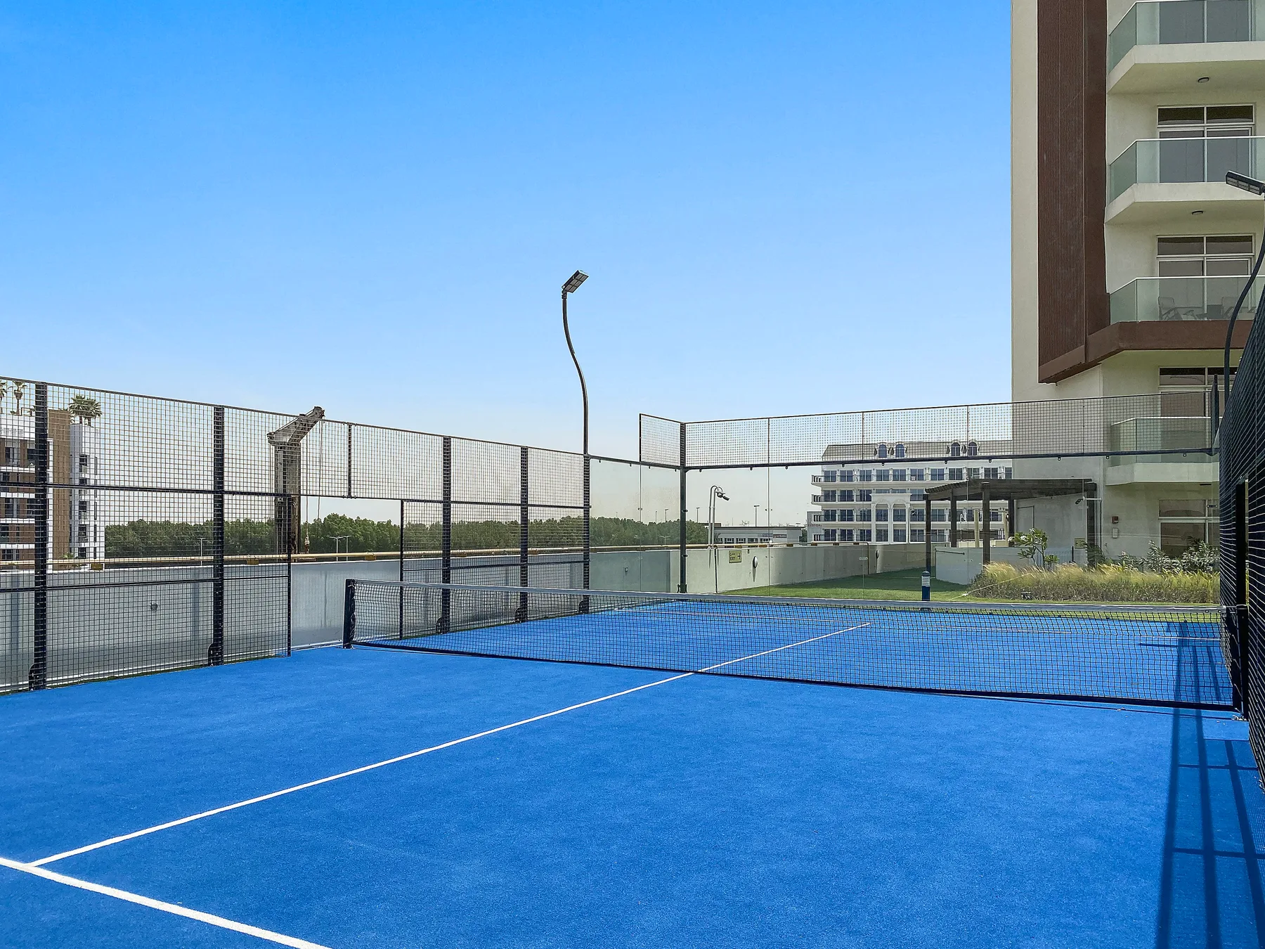 Una pista de tenis azul al aire libre está rodeada por una valla junto a un edificio moderno.