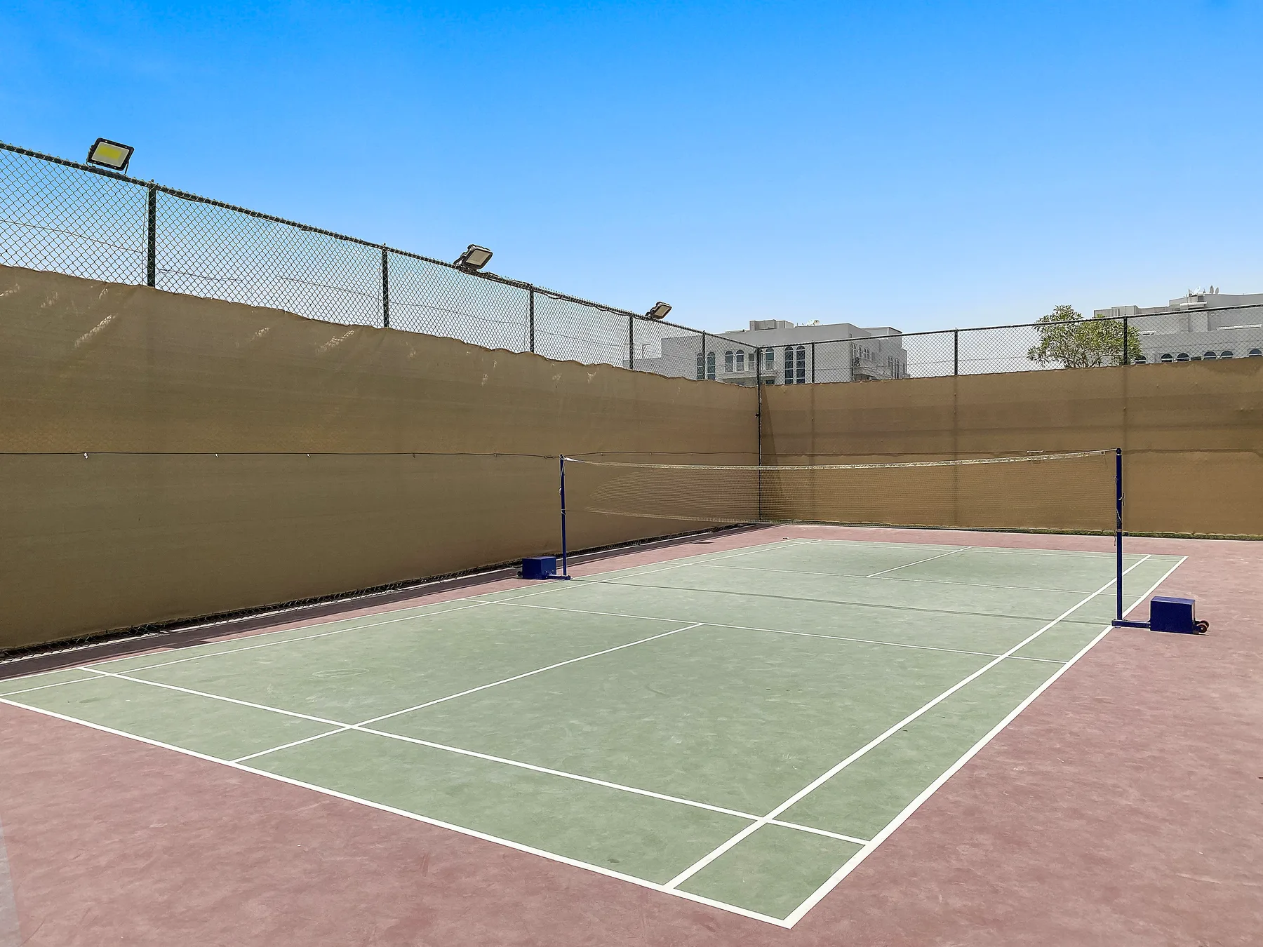 Una pista de tenis al aire libre está rodeada de cercas altas bajo un cielo despejado.