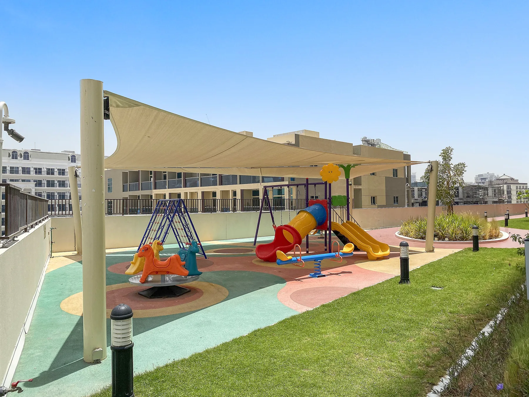 Un parque infantil al aire libre con toboganes y columpios de colores está bajo una lona de sombra.