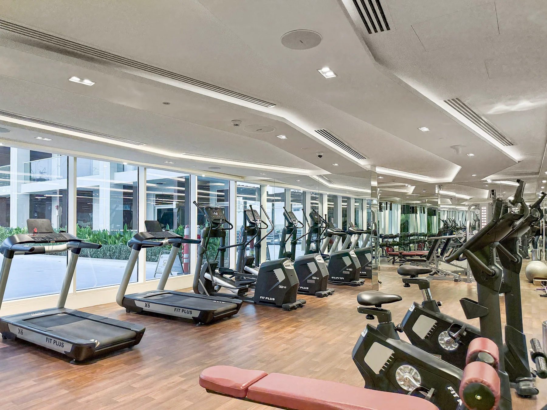 Una sala de ejercicio con máquinas y cintas de correr junto a grandes ventanas.