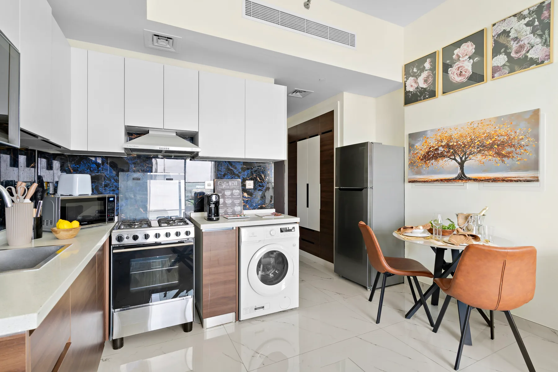 Una cocina compacta con zona de comedor, armarios blancos y una mesa pequeña.