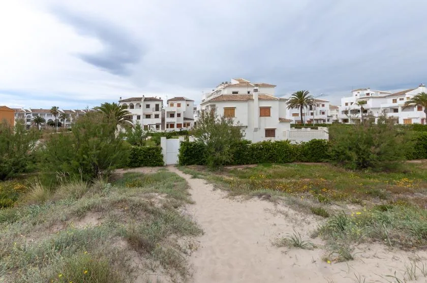 A sandy footpath runs through low vegetation toward white residential buildings.