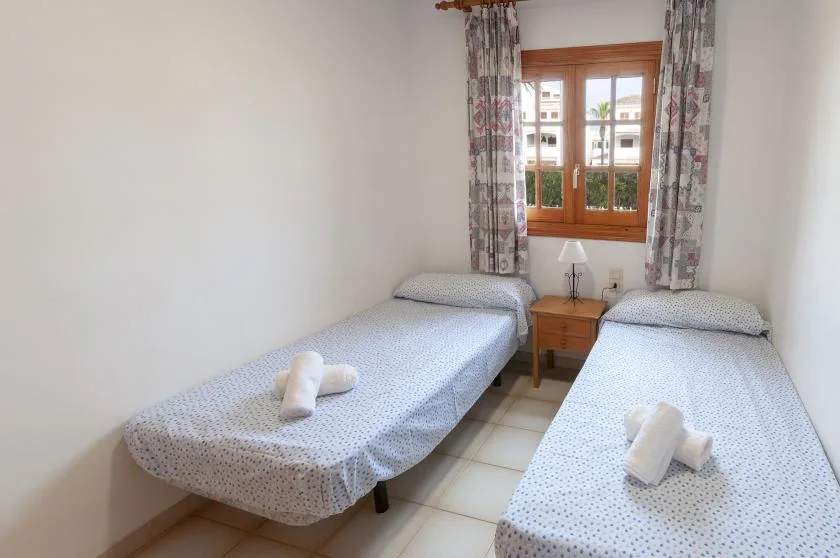 A twin bedroom with two single beds and a window between patterned curtains.