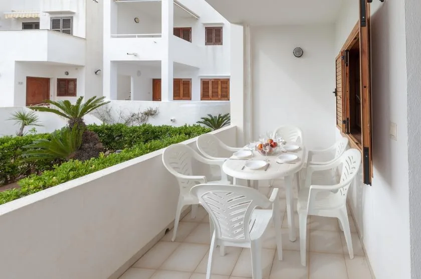 A balcony seating area with white plastic chairs and a table beside the garden.