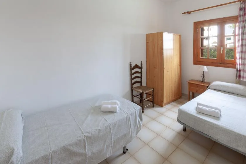 A bright bedroom with two beds, a wooden wardrobe, and a window.