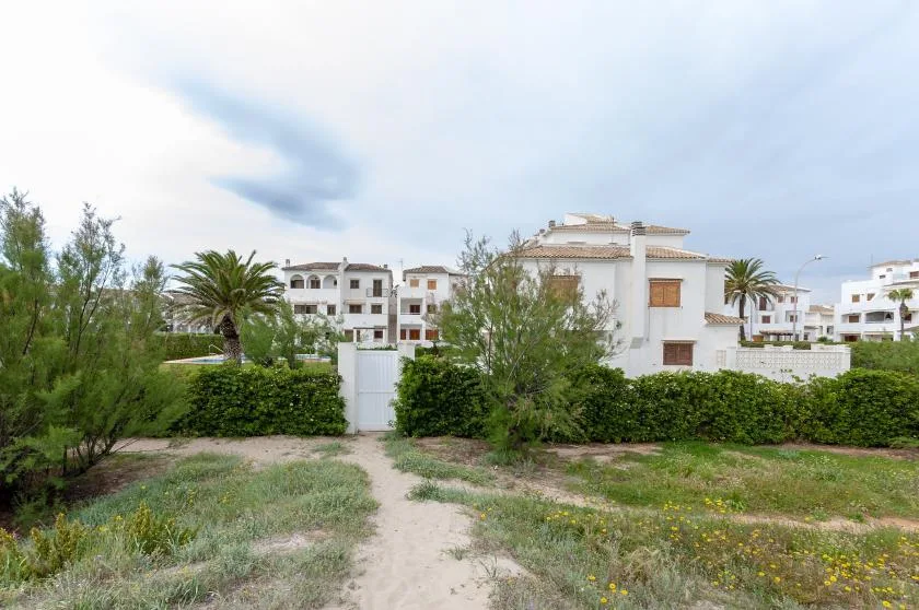 A sandy path leads through greenery toward white residential buildings.