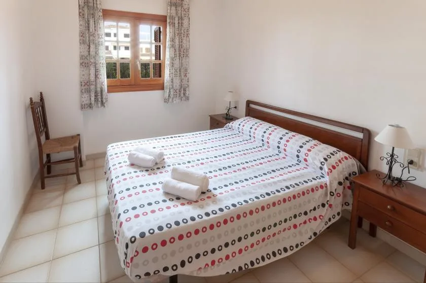 A bedroom with a double bed, patterned bedding, and a window with curtains.