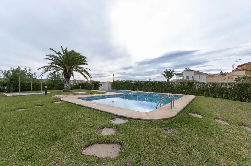 An outdoor swimming pool sits in a grassy garden beneath a cloudy sky.