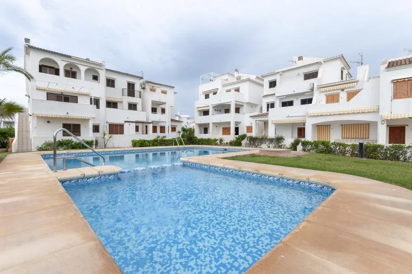 An outdoor swimming pool sits among white residential buildings and landscaped grounds.