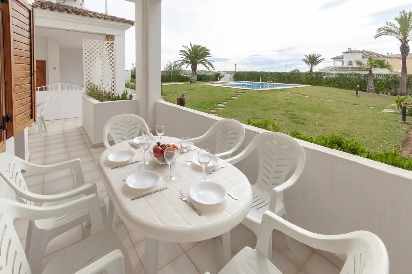 A covered patio with outdoor seating overlooks a lawn and swimming pool.