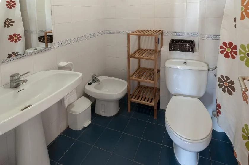 A tiled bathroom with a bathtub, sink, toilet, and wooden shelving.