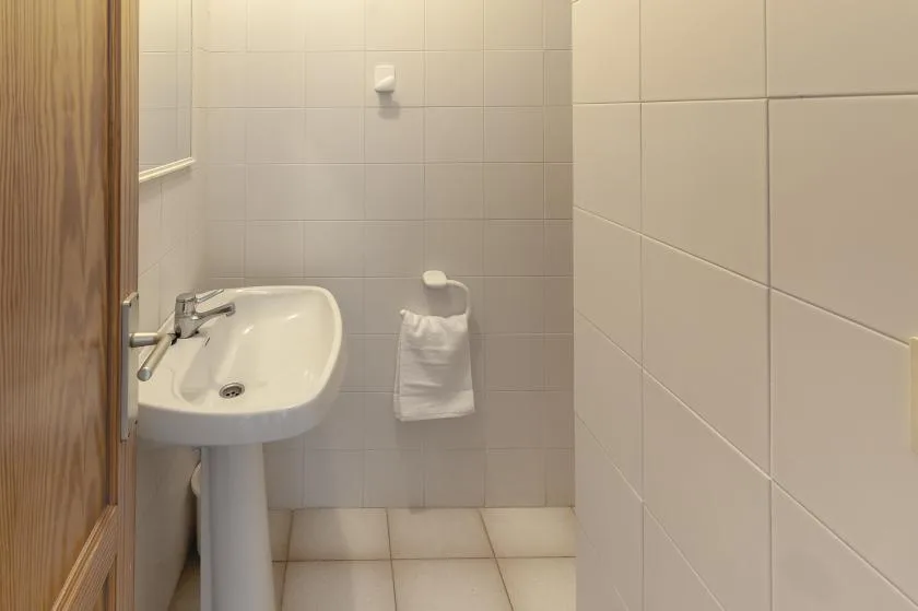 A tiled bathroom with a pedestal sink and a towel hanging on the wall.
