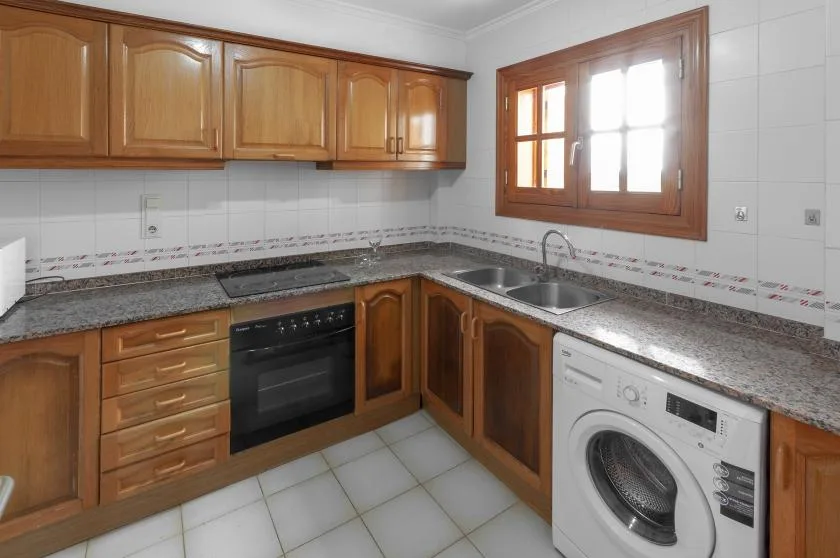 A tiled kitchen with wooden cabinets, a sink, and a washing machine.